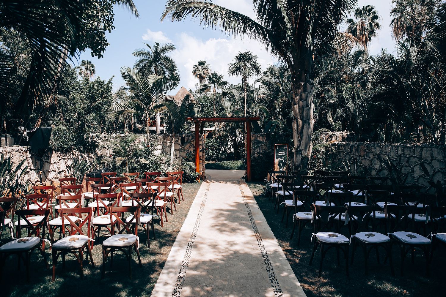 Outdoor wedding ceremony setup with rows of chairs along a stone pathway surrounded by tropical palm trees.