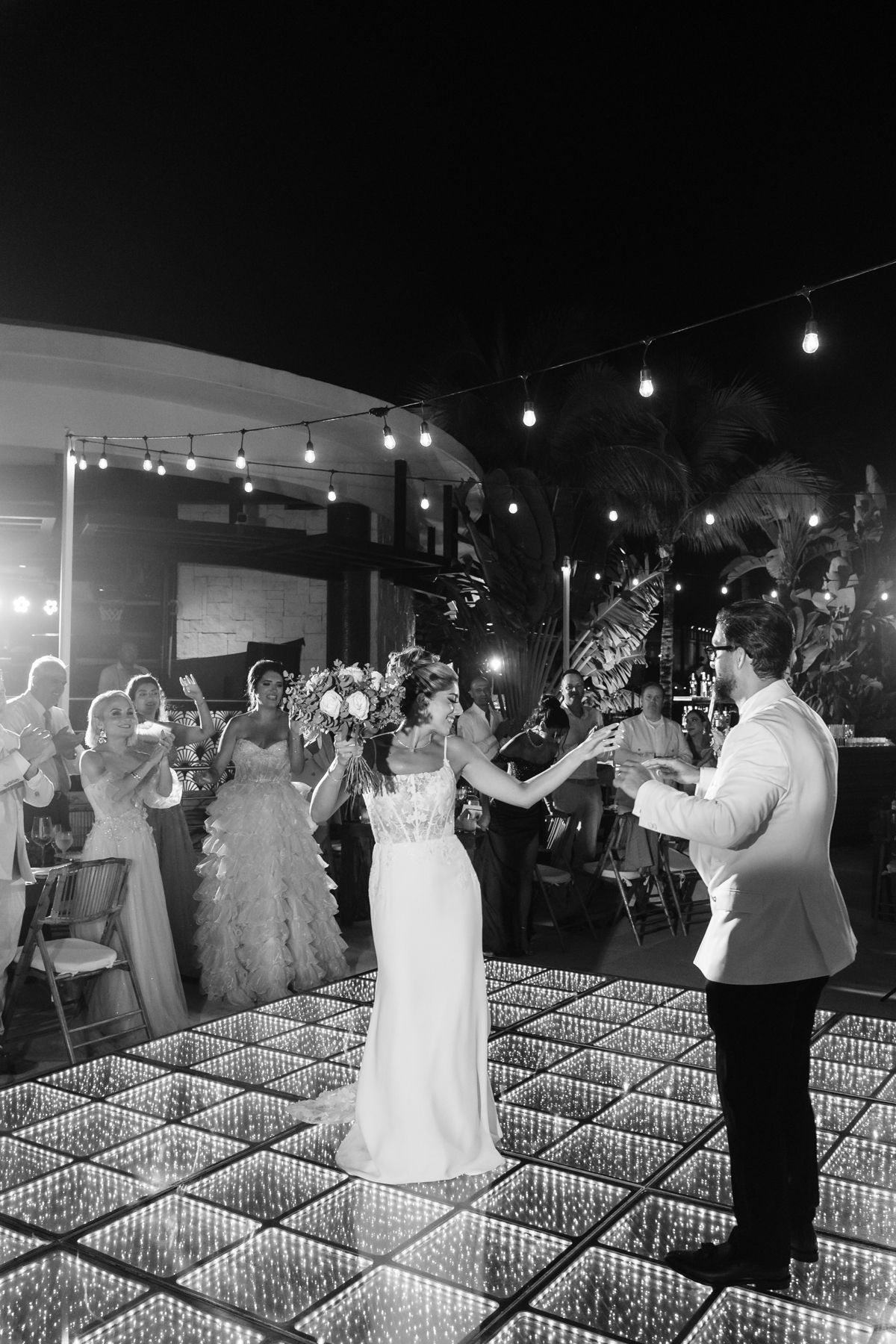 Bride and groom dance on a sparkling illuminated floor at an elegant outdoor evening wedding reception.