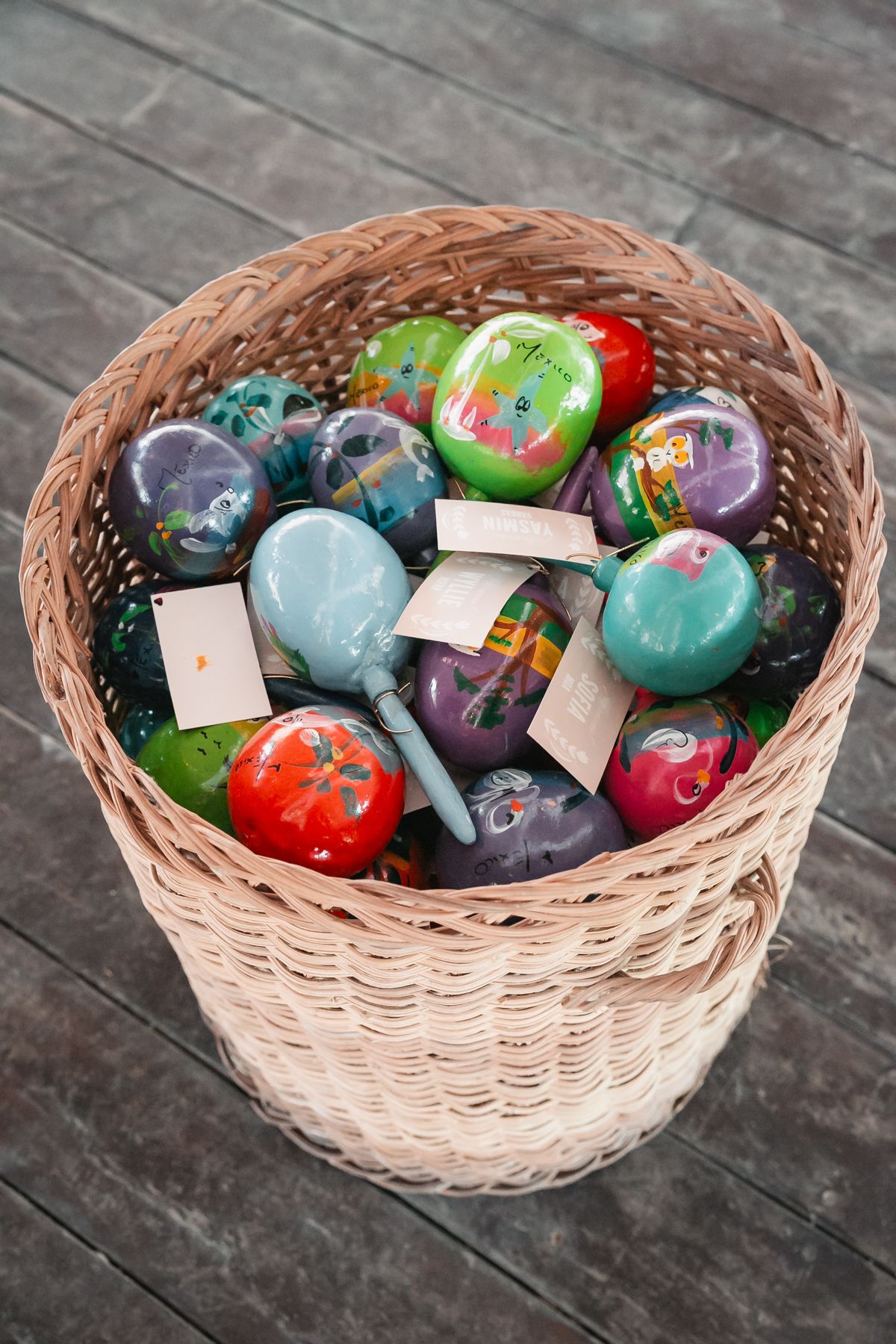 Colorful painted Easter eggs and maracas in a large woven wicker basket on a wooden deck.