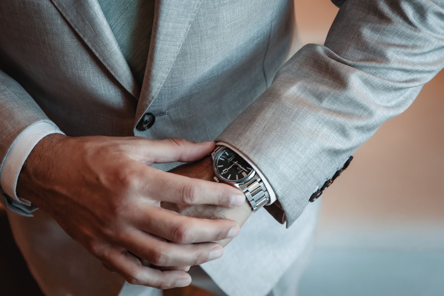 Man in light gray suit adjusting a brown leather strap luxury wristwatch on his wrist.