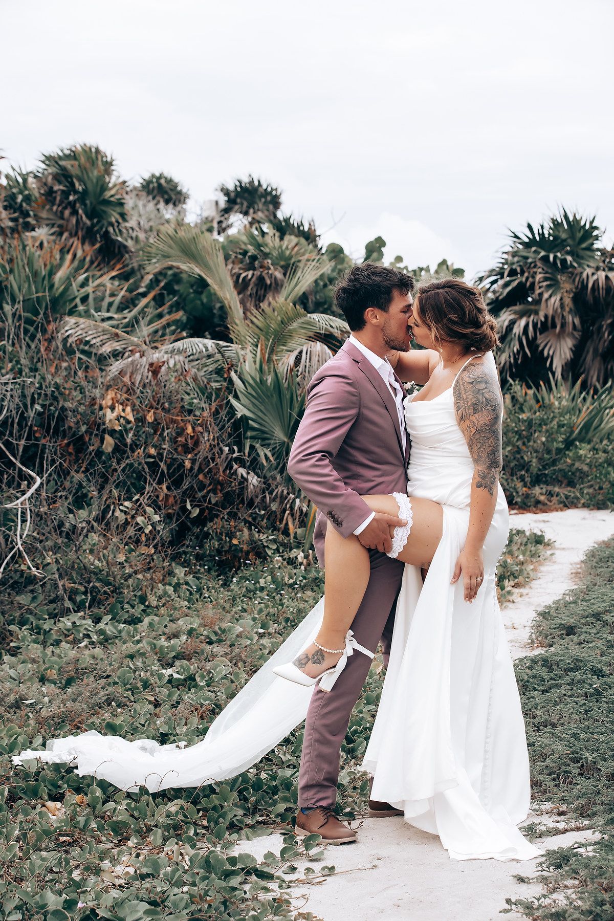 A romantic wedding photoshoot showing a couple dancing and embracing on a tropical garden path with flowing white dress.