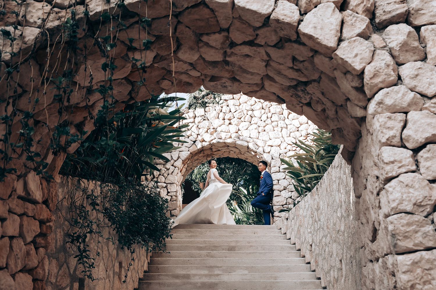Stone archways frame a dramatic bridal portrait with flowing white dress train.
