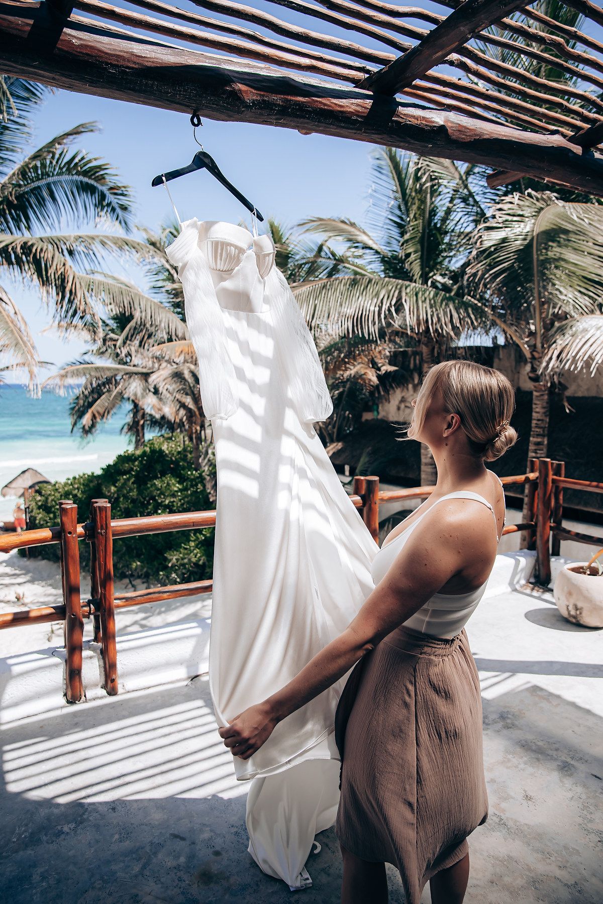 Wedding dress hanging against beachfront backdrop with palm trees and ocean view.