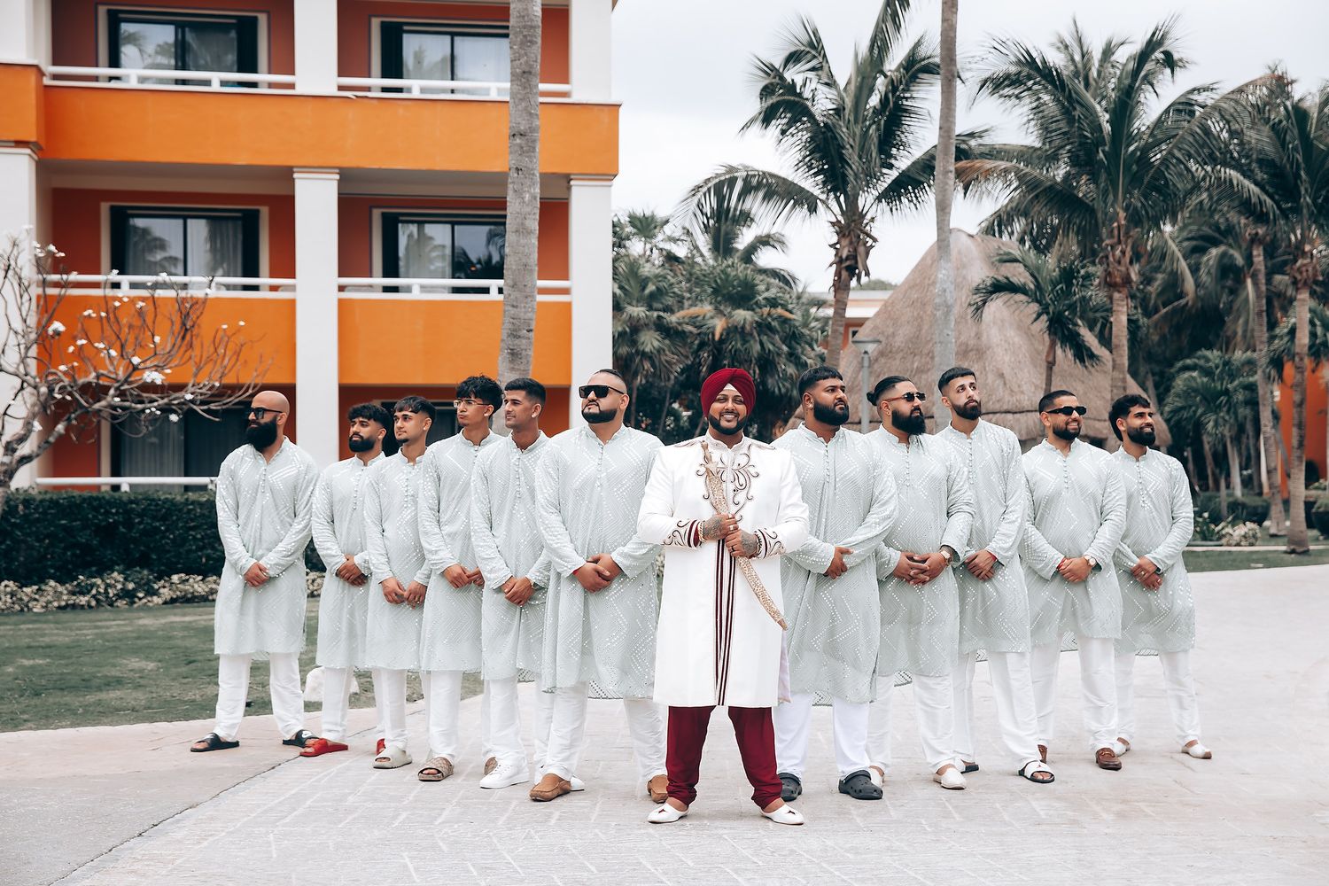 Groomsmen in matching white outfits with groom in burgundy at tropical resort.