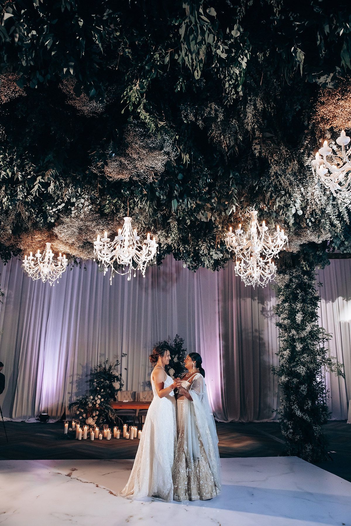 Romantic wedding ceremony setup with white draping, chandeliers, and overhead greenery creating an enchanted atmosphere.