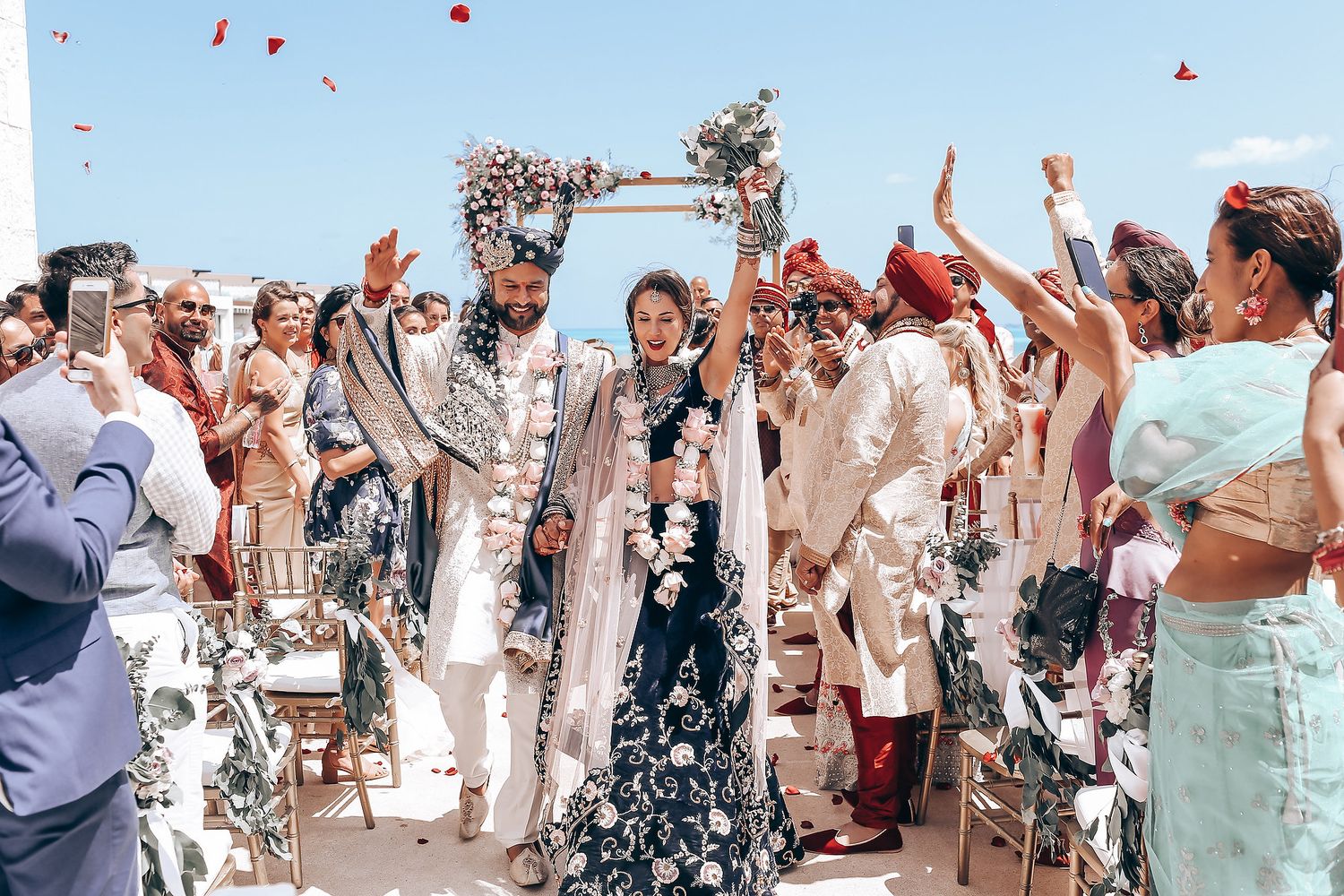 Joyful crowd throws petals during a beachside wedding celebration.
