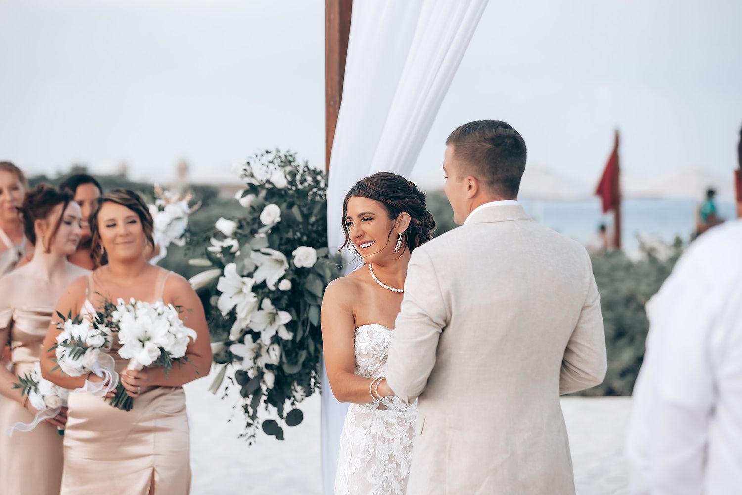 Wedding ceremony setup with white draping and floral arrangements on beach.