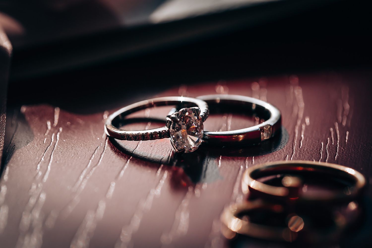 Close-up of elegant diamond engagement and wedding rings on dark textured surface.