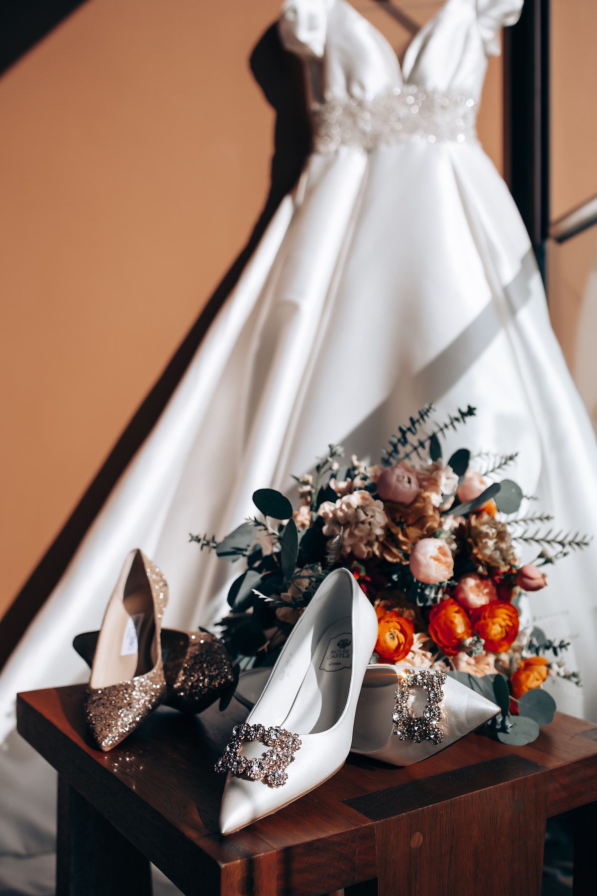 White wedding dress and bridal accessories arranged with orange and pink floral bouquets.