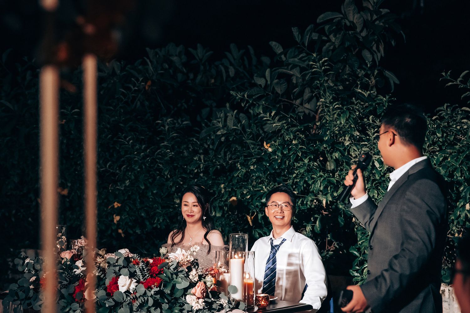 Evening wedding reception under string lights with tropical foliage.