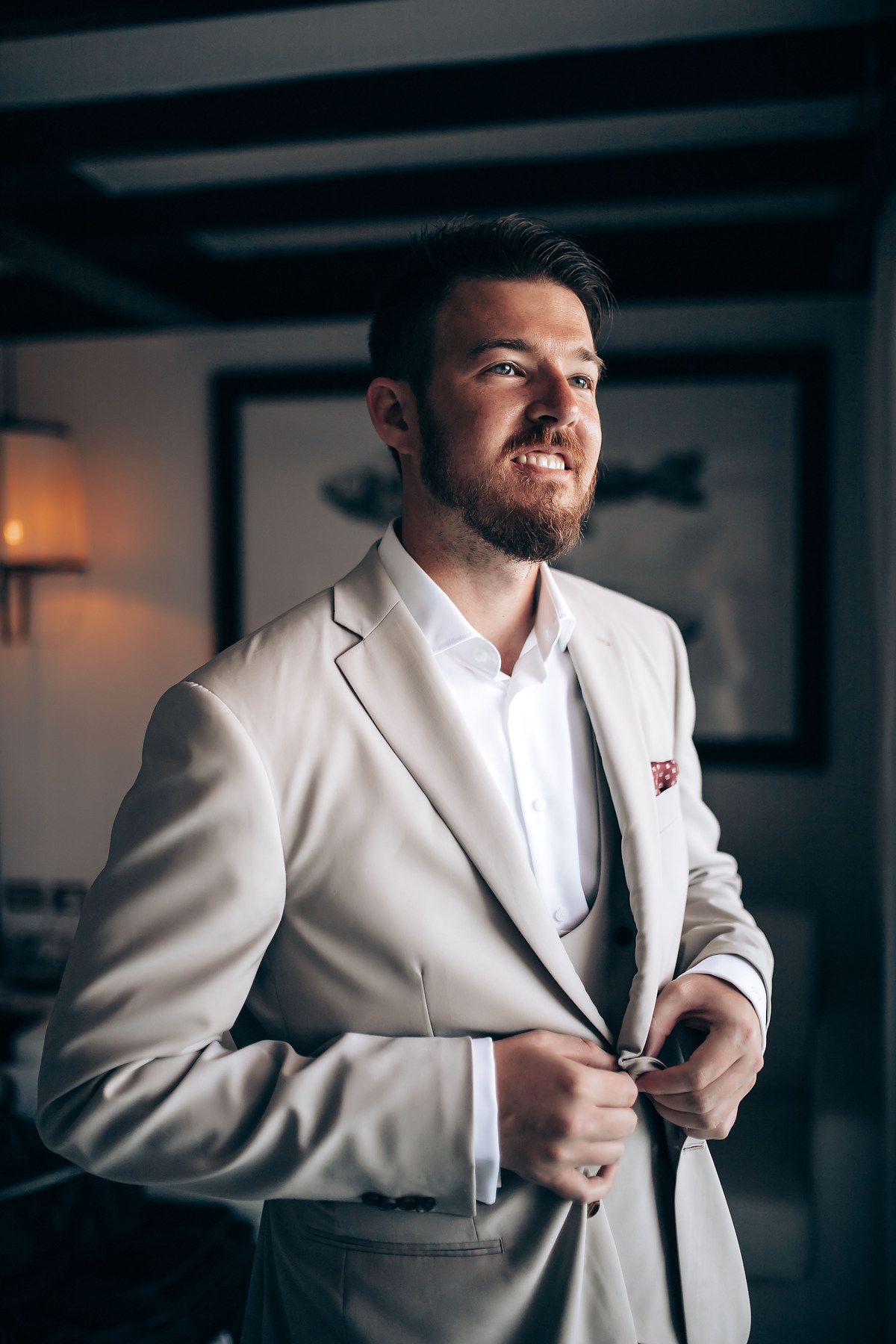 Series of photos showing groom adjusting light colored suit jacket in moody indoor setting.