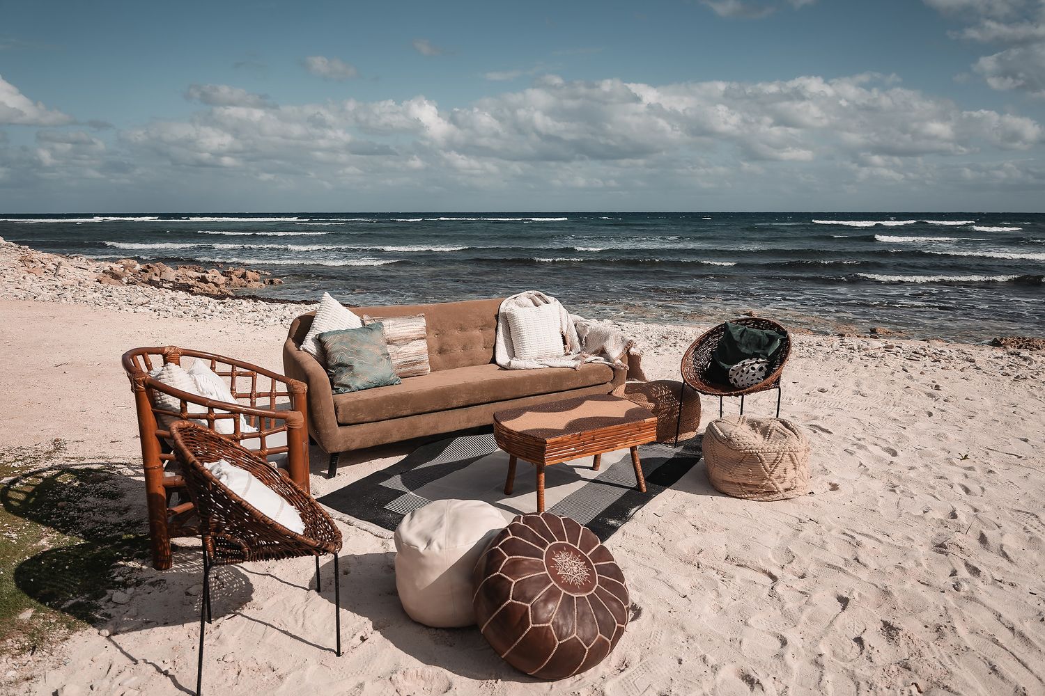 Wooden lounge furniture arranged on a pristine beach with ocean views and cloudy skies.