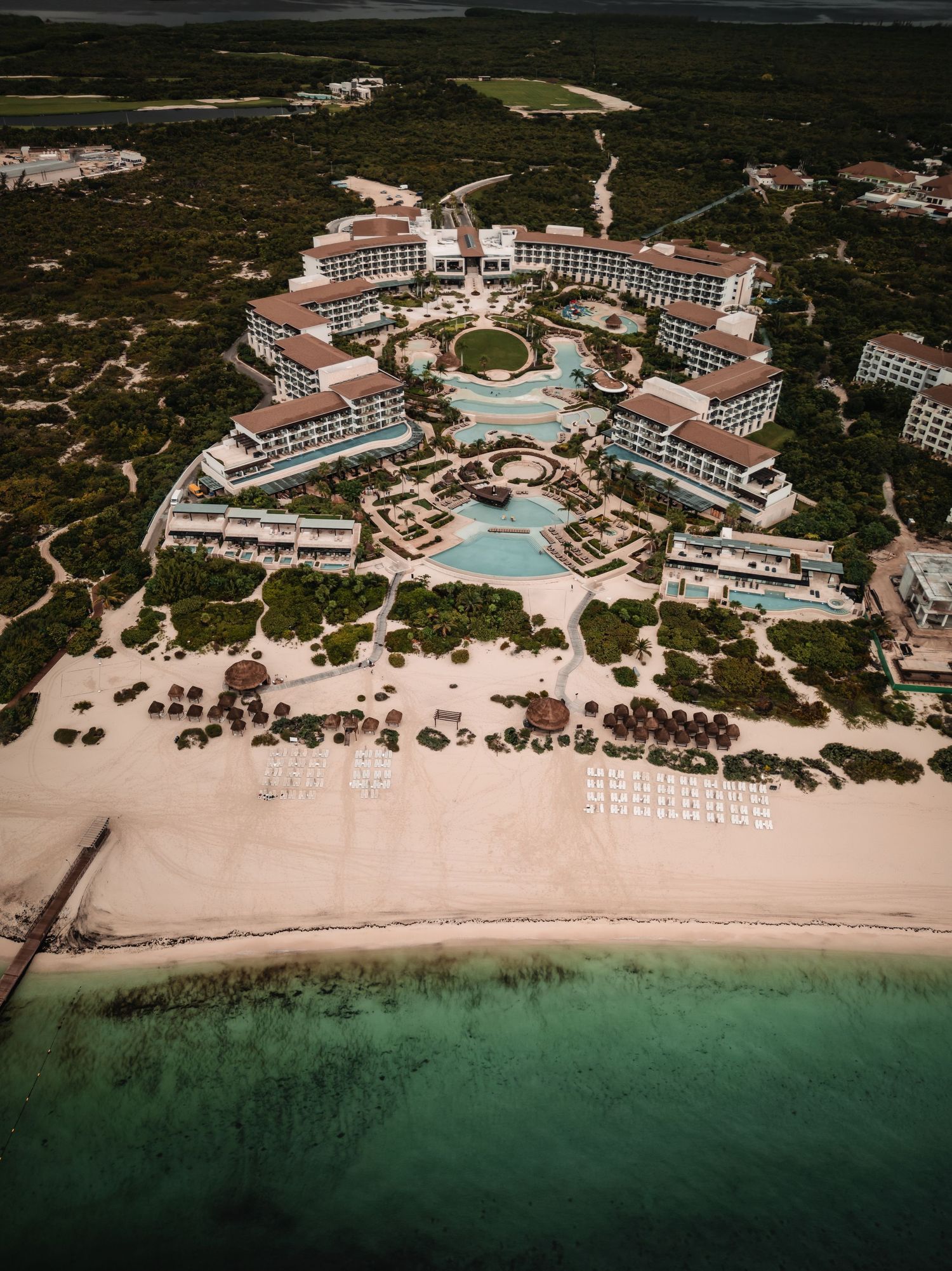 Drone shot of a sprawling beachfront resort complex with multiple pools and white sand beach.