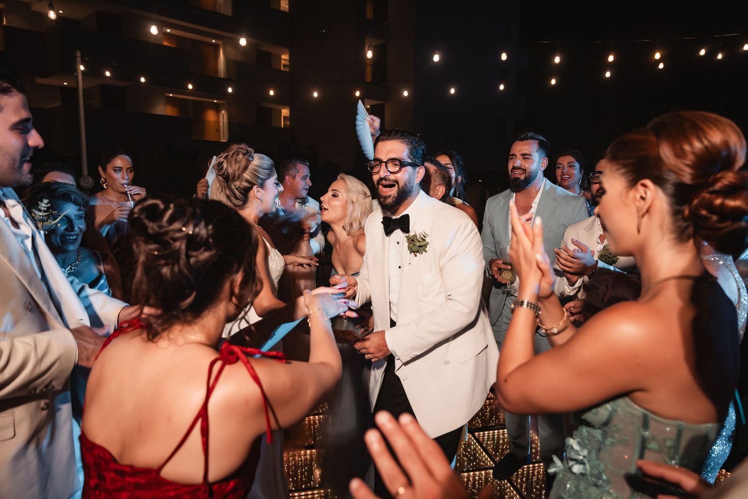Lively reception dance floor with guests celebrating under warm string light ambiance.
