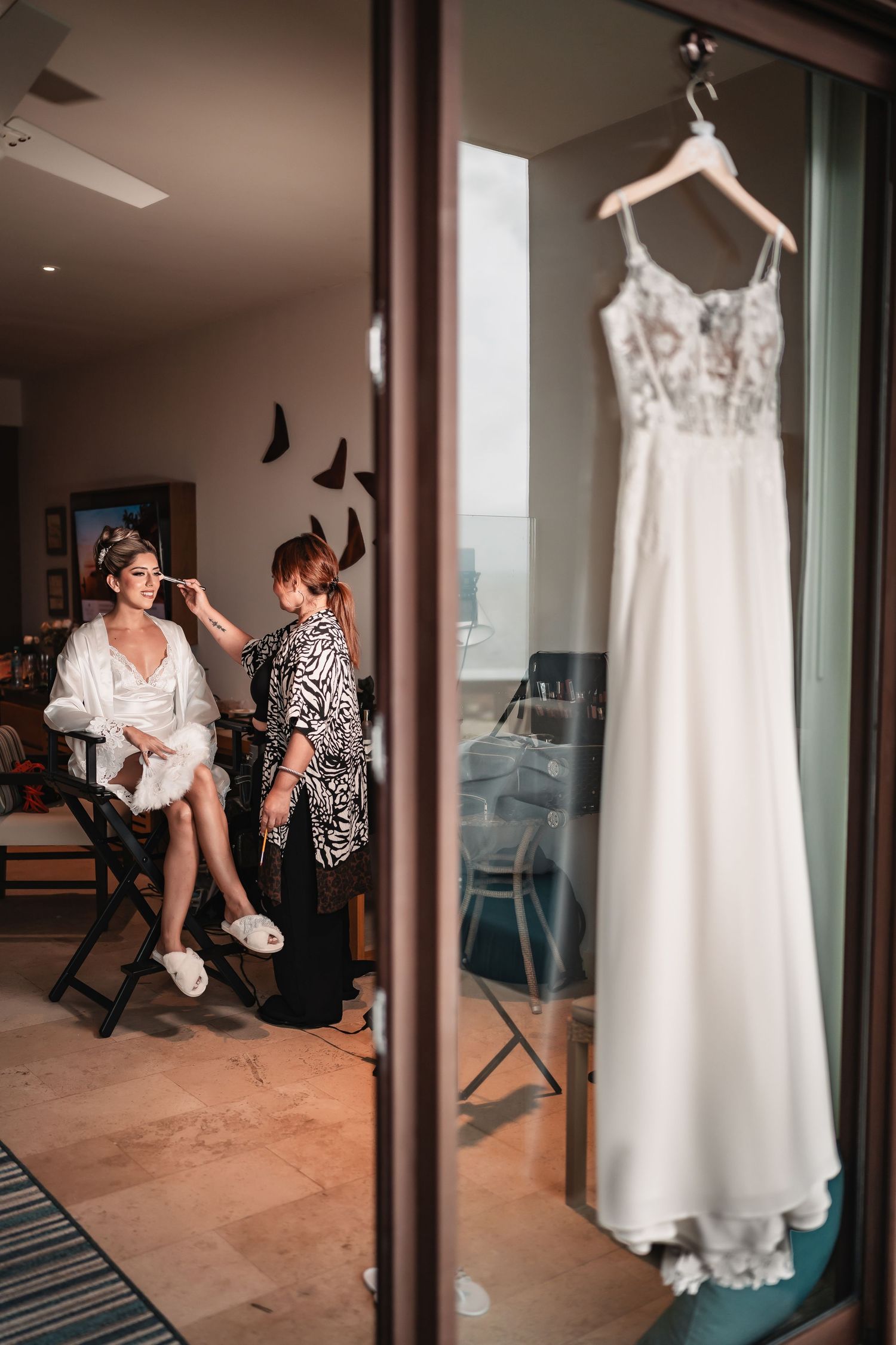 Wedding preparation room with white dress hanging and reflections in glass windows.