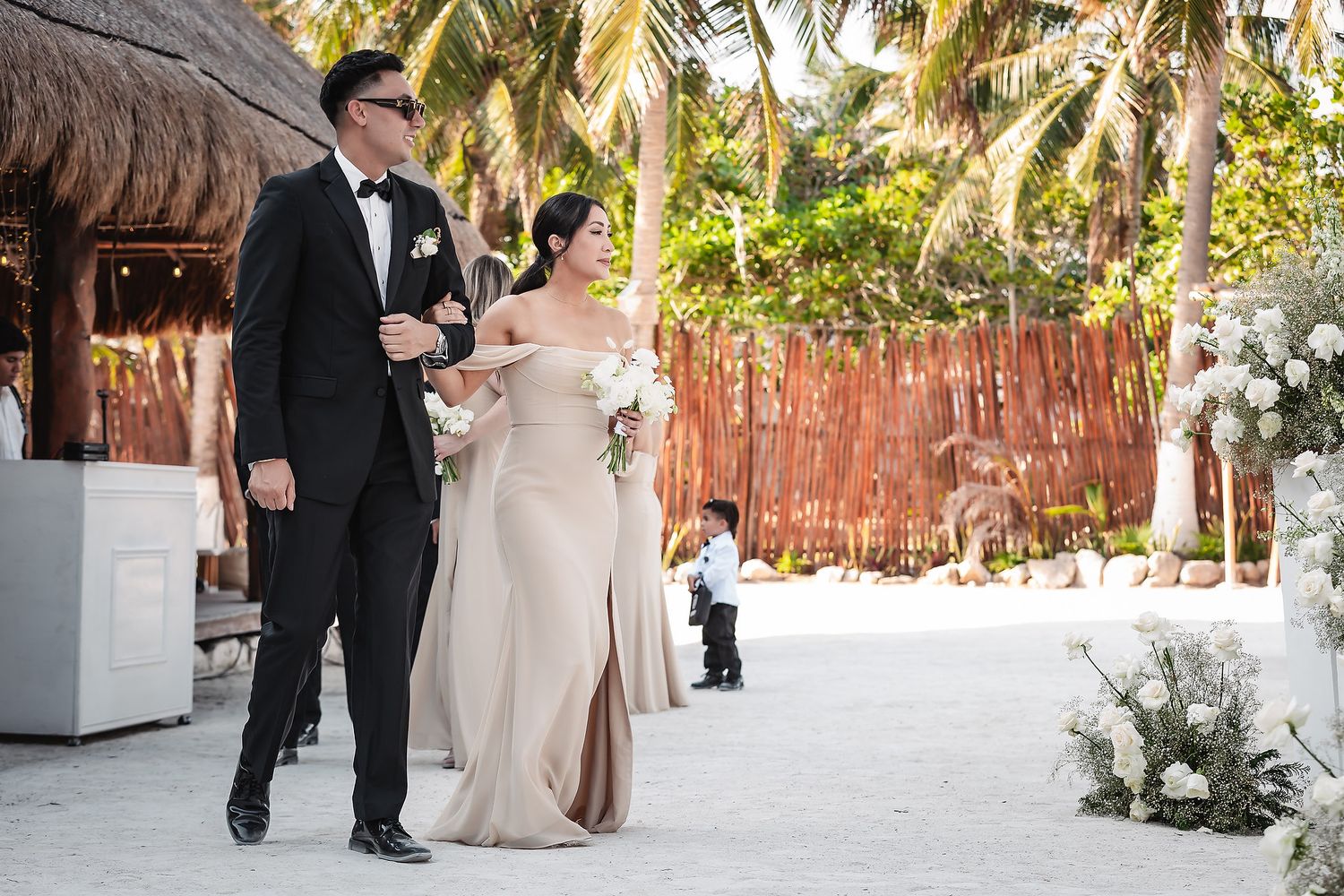 Wedding guests mingling on a white aisle runner with tropical palm trees in background.