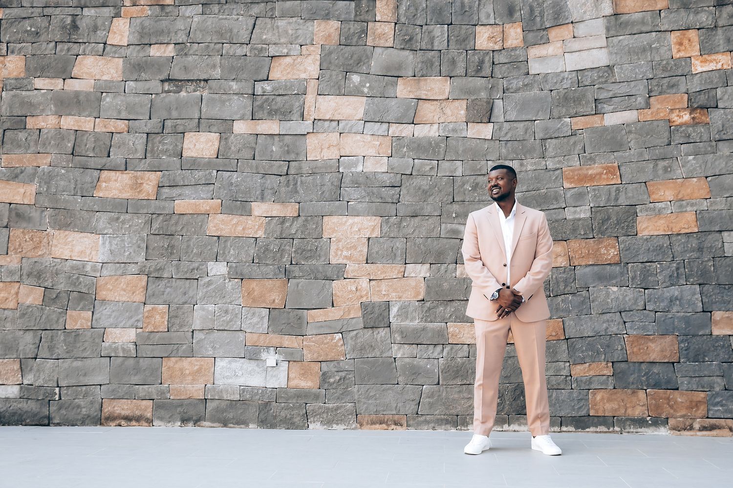 Person in formal attire sitting on stone steps against a textured stone wall background.