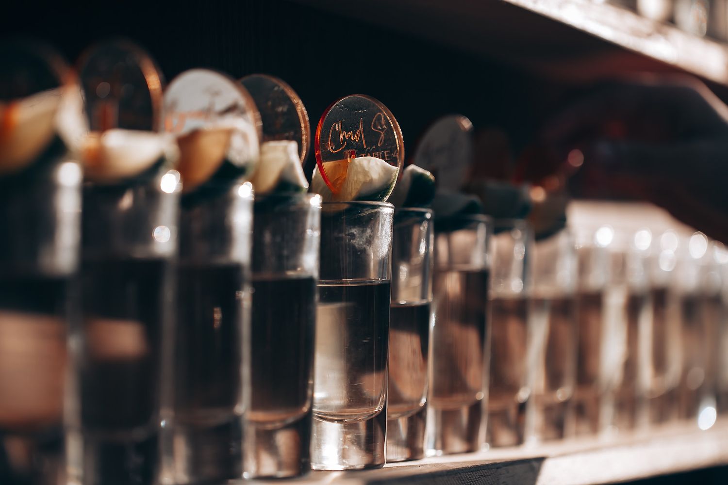 Elegant cocktail glasses and bar equipment arranged on a dark wooden counter in soft lighting.