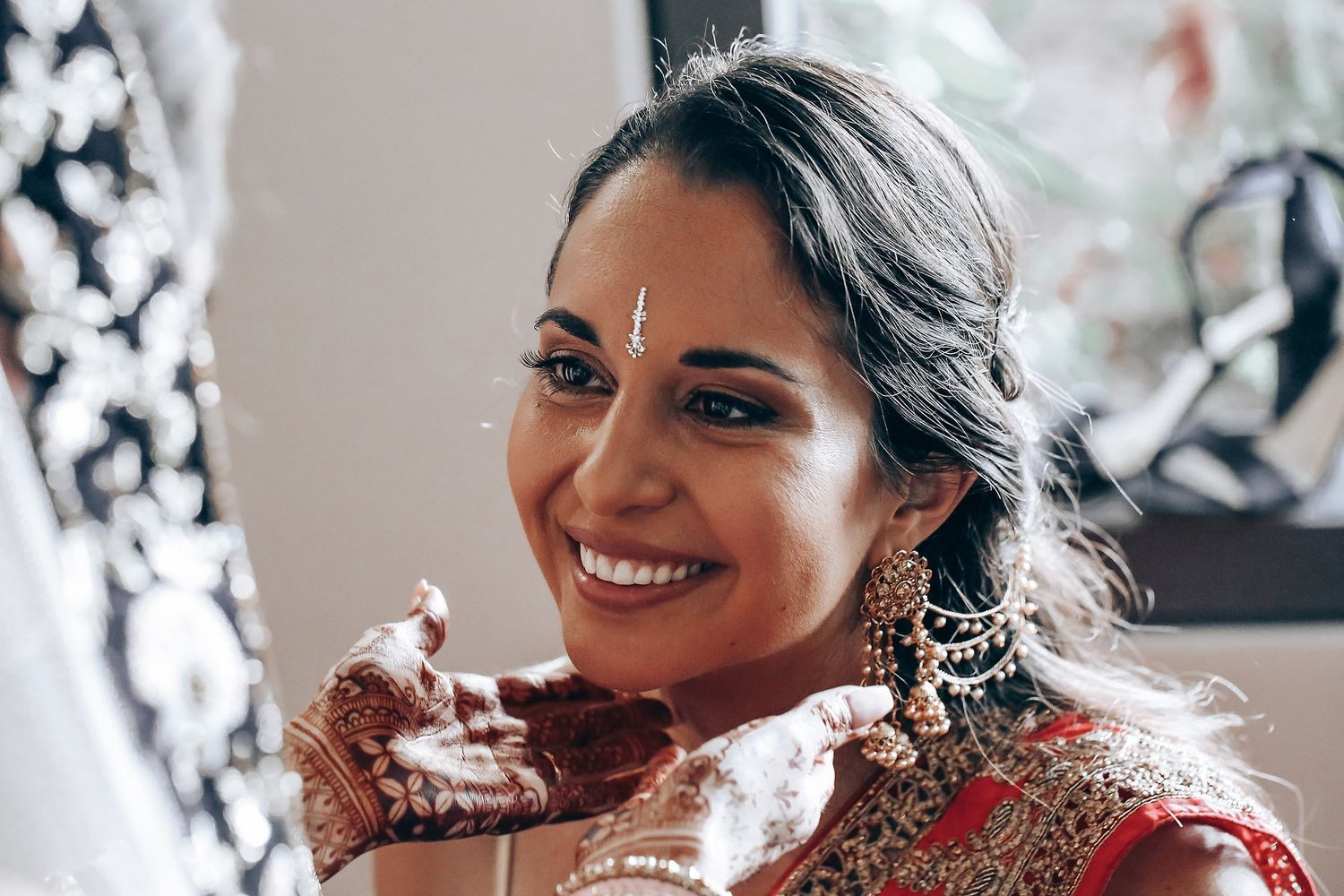 A bride in a red and gold Indian wedding lehenga smiles while enjoying a sweet dessert.