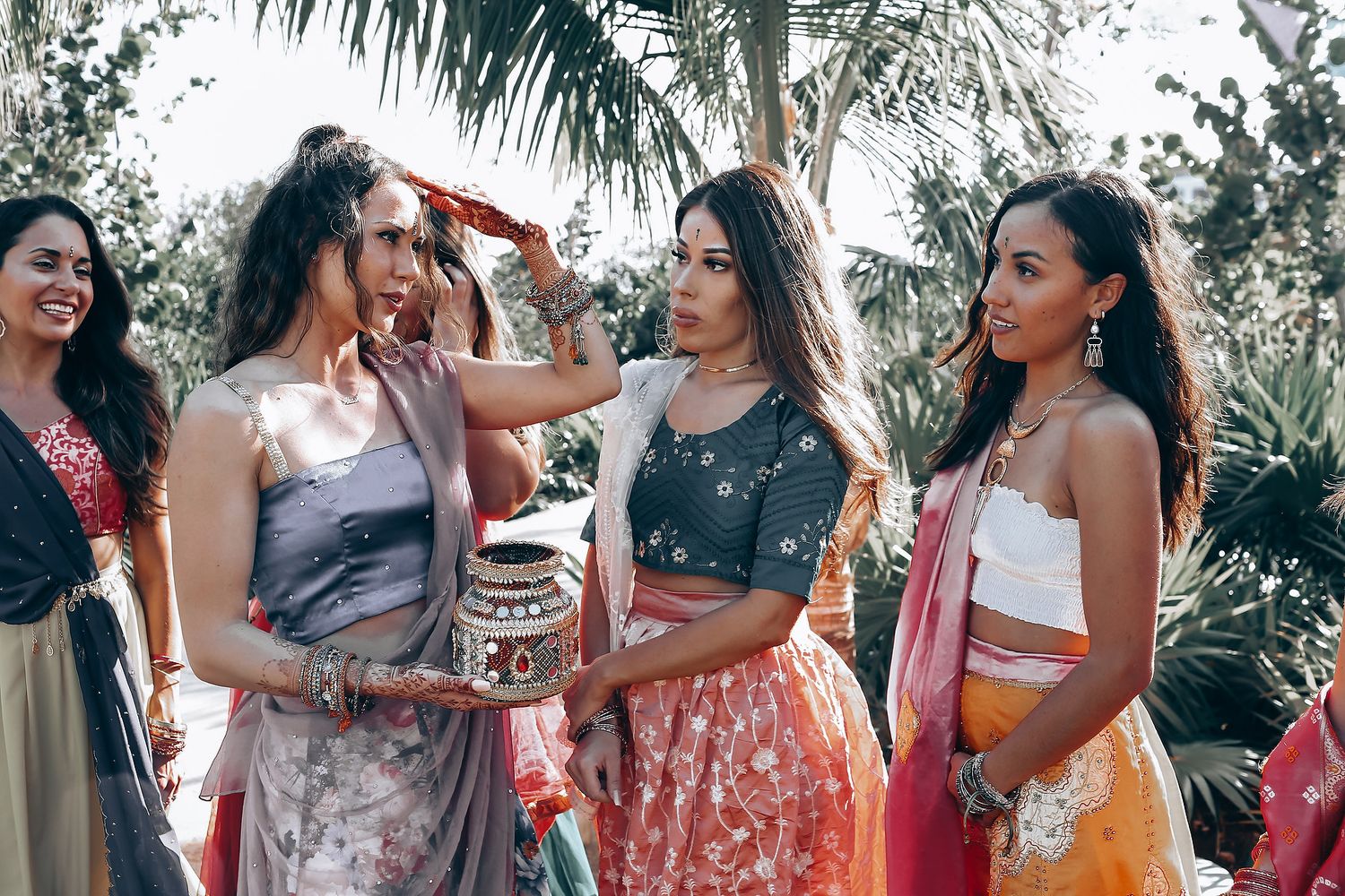 A group of friends in colorful dresses laugh and socialize at an outdoor tropical garden party.