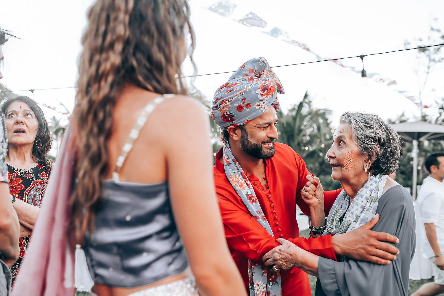 Group of people dancing and celebrating together at an outdoor party with string lights overhead.