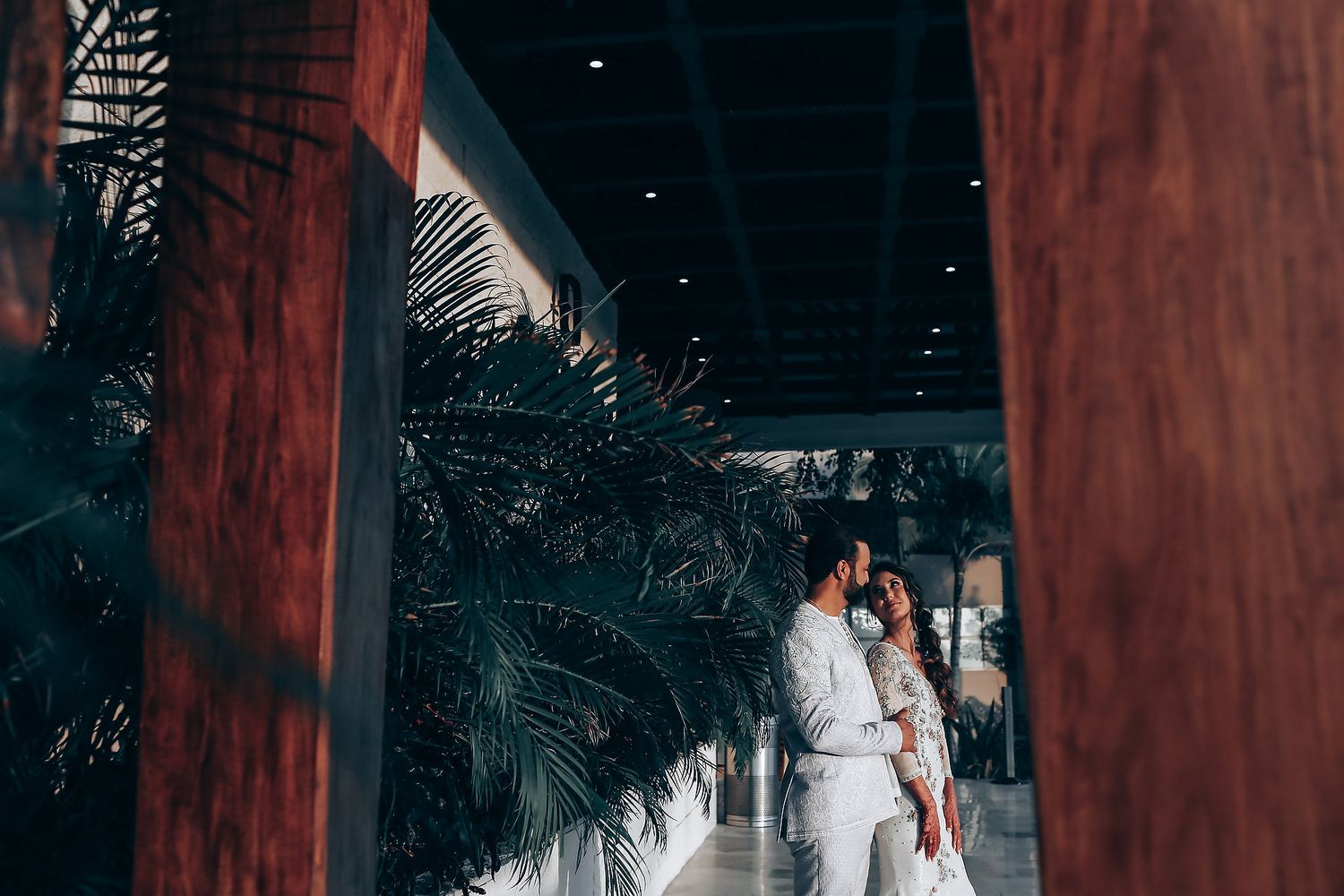 A couple embraces in a rustic wooden gazebo with tropical greenery in the background during a romantic moment.