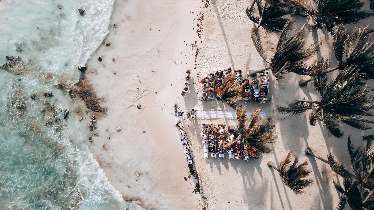 Decorative palm fronds and tropical foliage arrangements create a natural beach wedding setting.