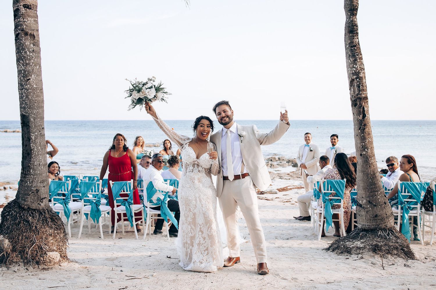 A beachside celebration with palm trees and turquoise chairs set up along the sandy shore.