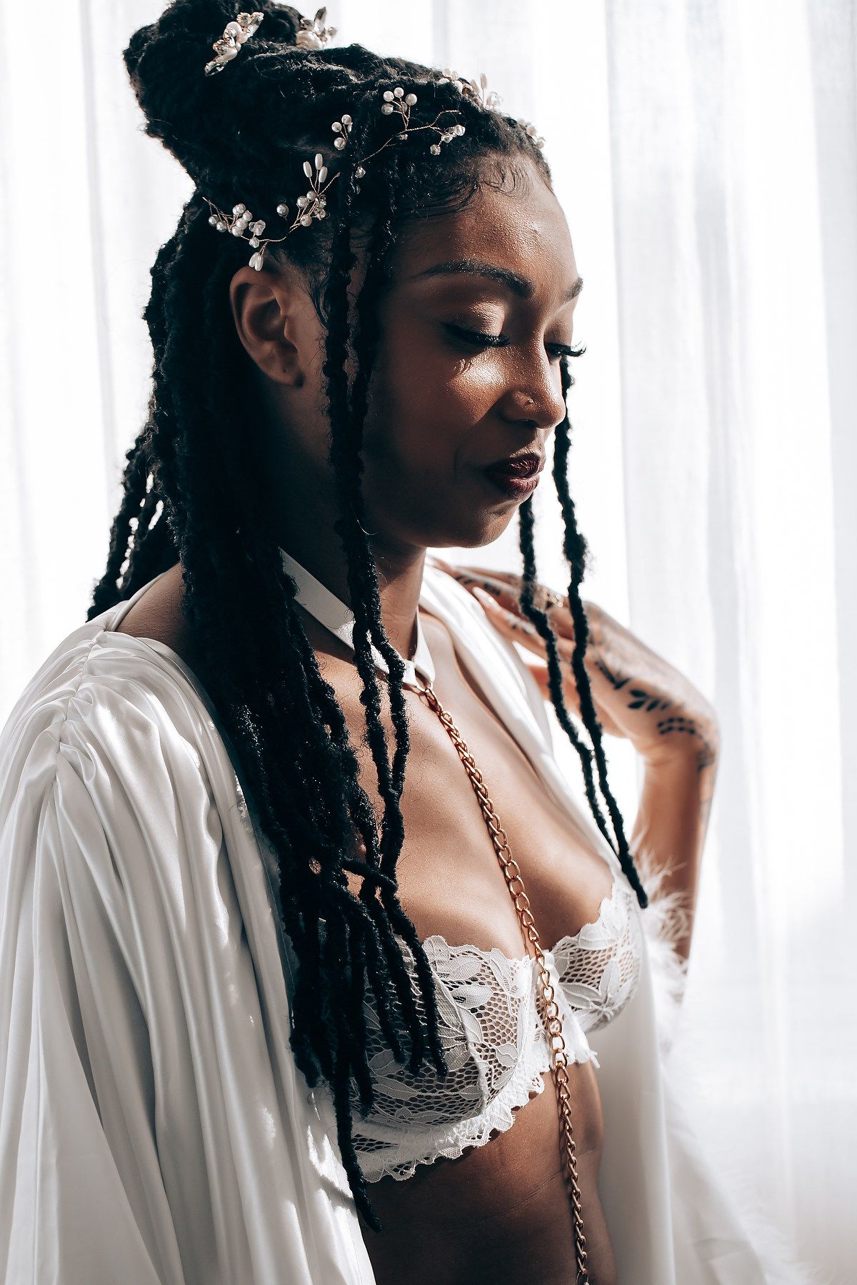 A portrait showing long braided hair adorned with delicate floral accessories and white lace lingerie.