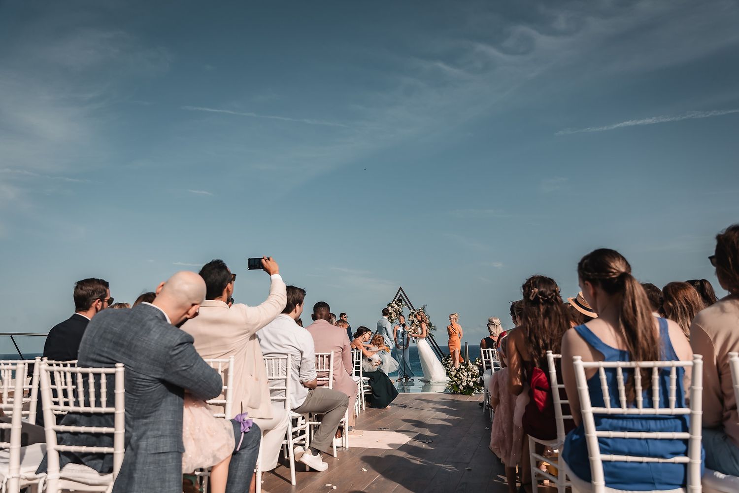 Panoramic view of beach wedding ceremony setup with white chairs and ocean backdrop.