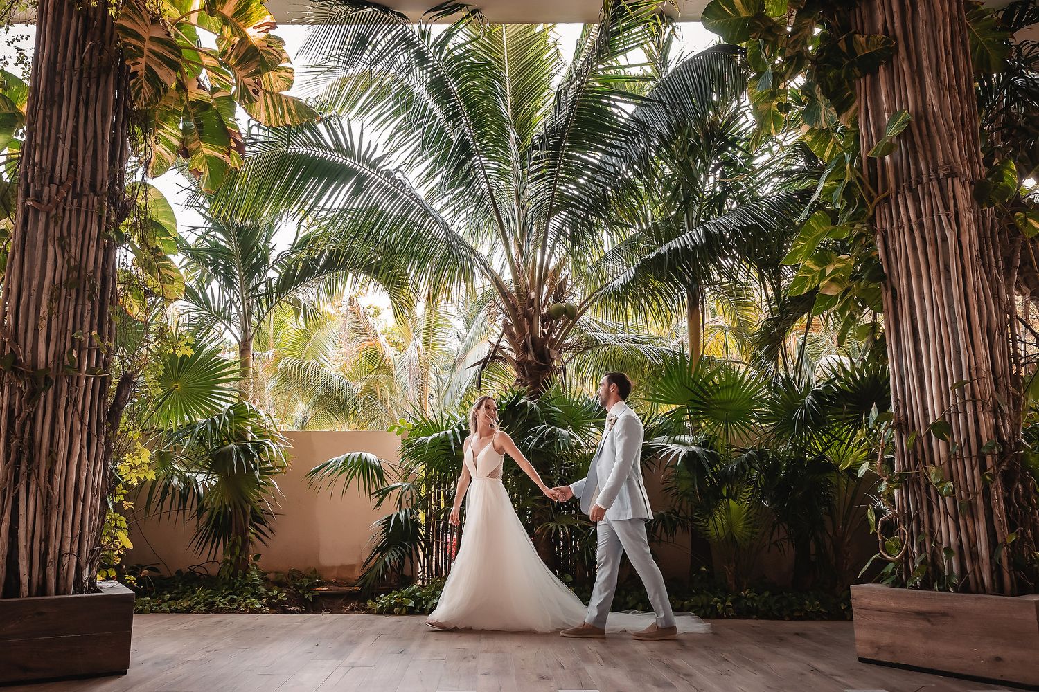 A sunlit garden walkway with palm trees creates a romantic backdrop for a couple.
