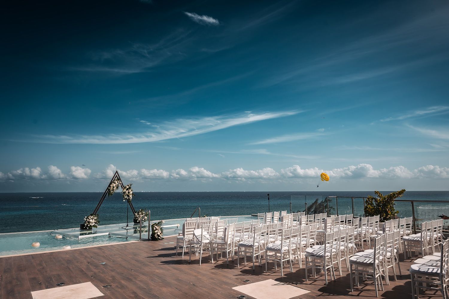 Beachfront wedding setup with white chairs and wooden altar against turquoise waters.