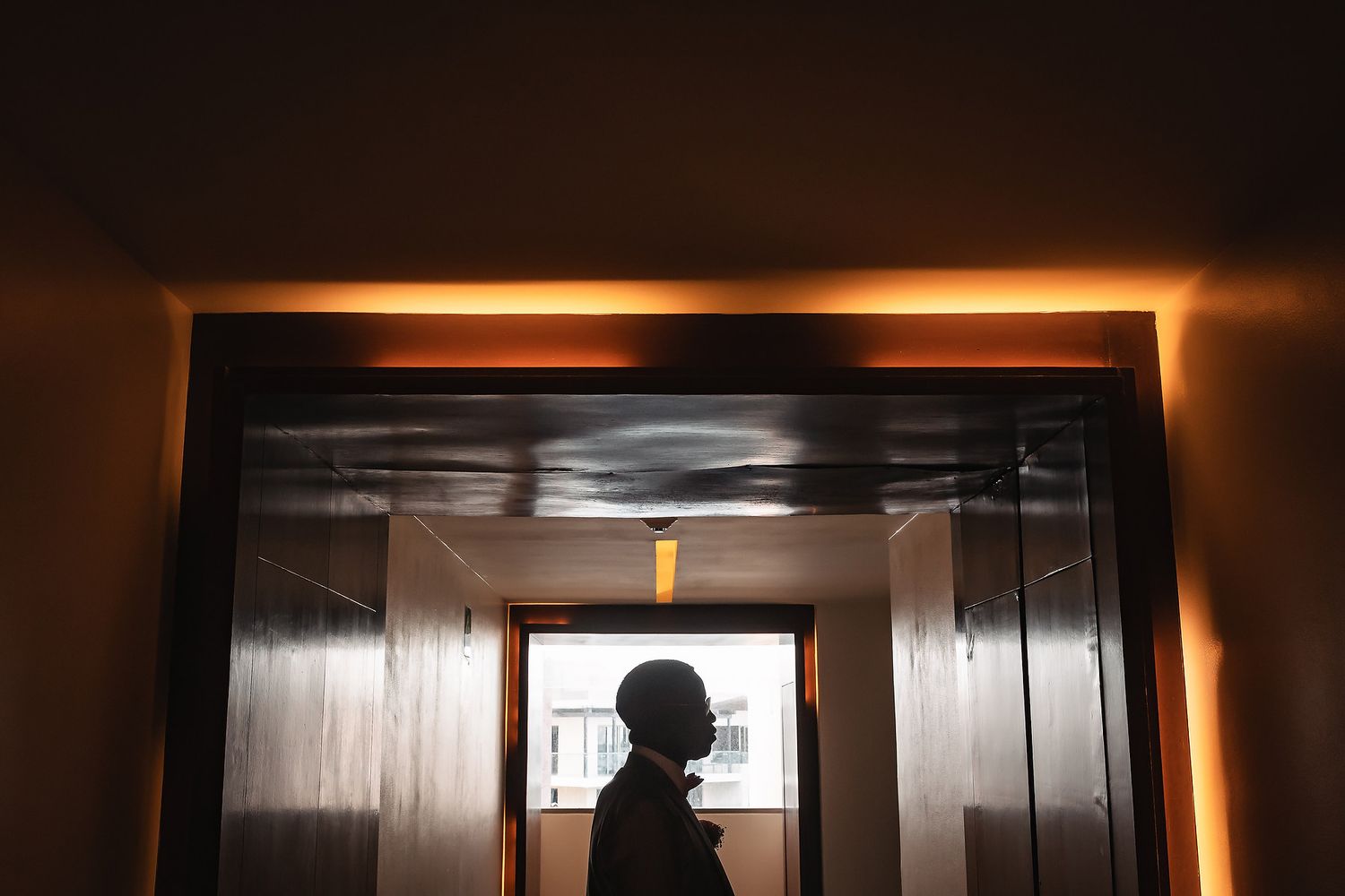 Silhouette of a person standing in a dimly lit hallway with orange ambient lighting.