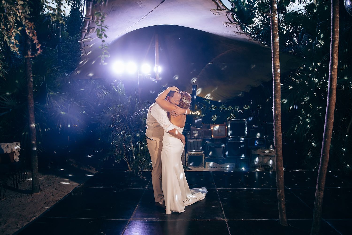 Romantic dance scene captured at twilight under outdoor wedding tent lighting.