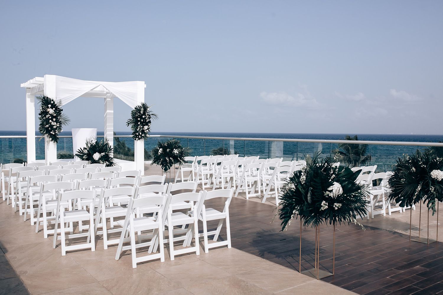 White chairs arranged in rows on an outdoor deck overlooking the ocean for a seaside ceremony.