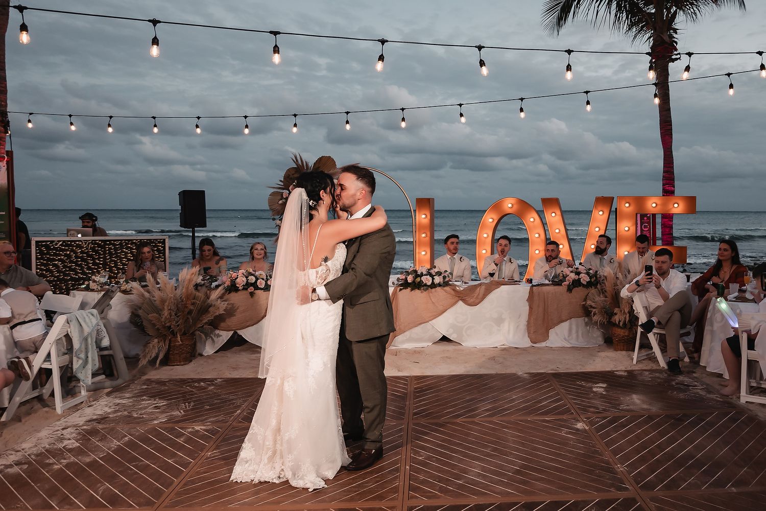 String lights illuminate a beachfront wedding reception as the sun sets.