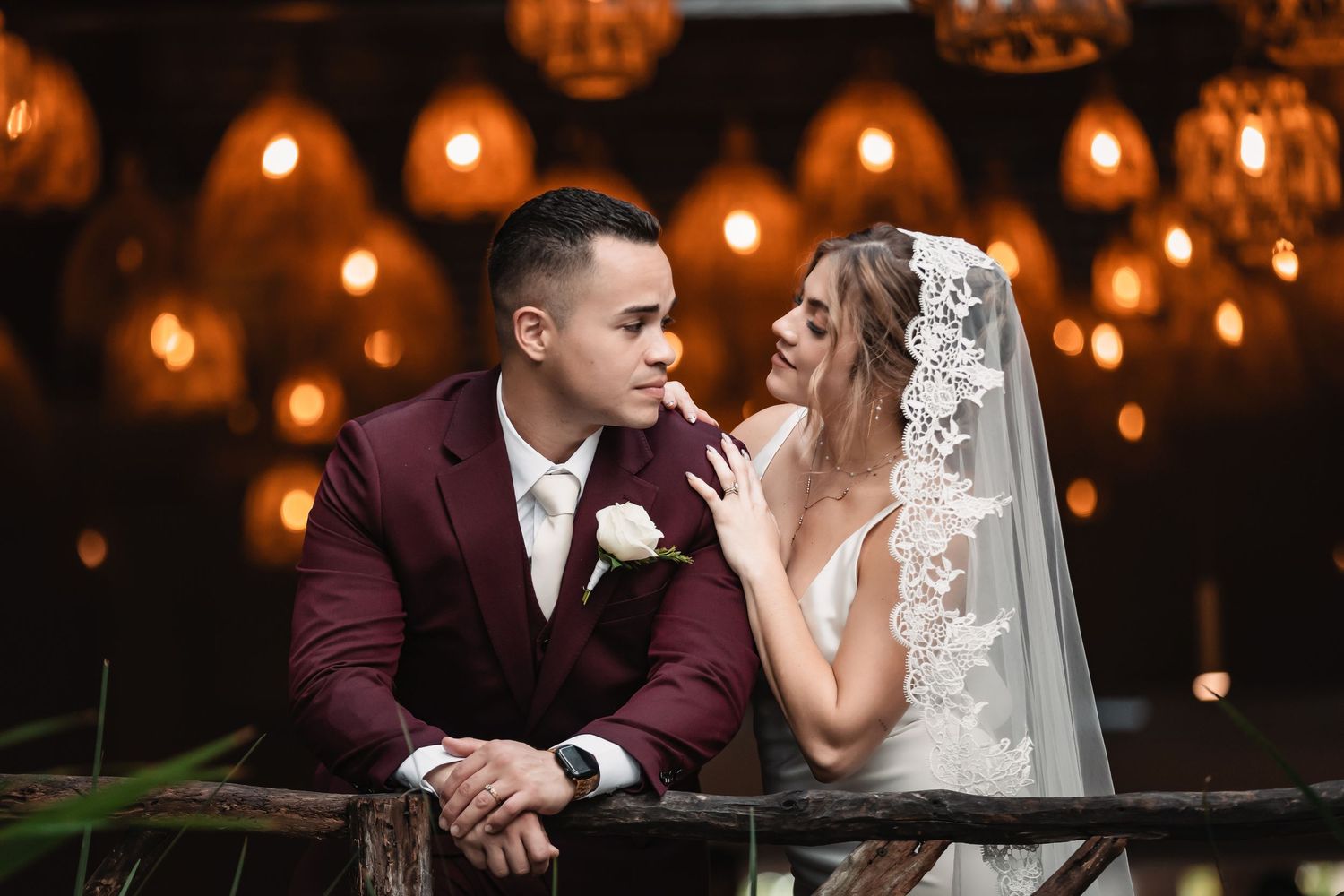 Romantic wedding couple shares intimate moment under warm glowing string lights at evening reception.