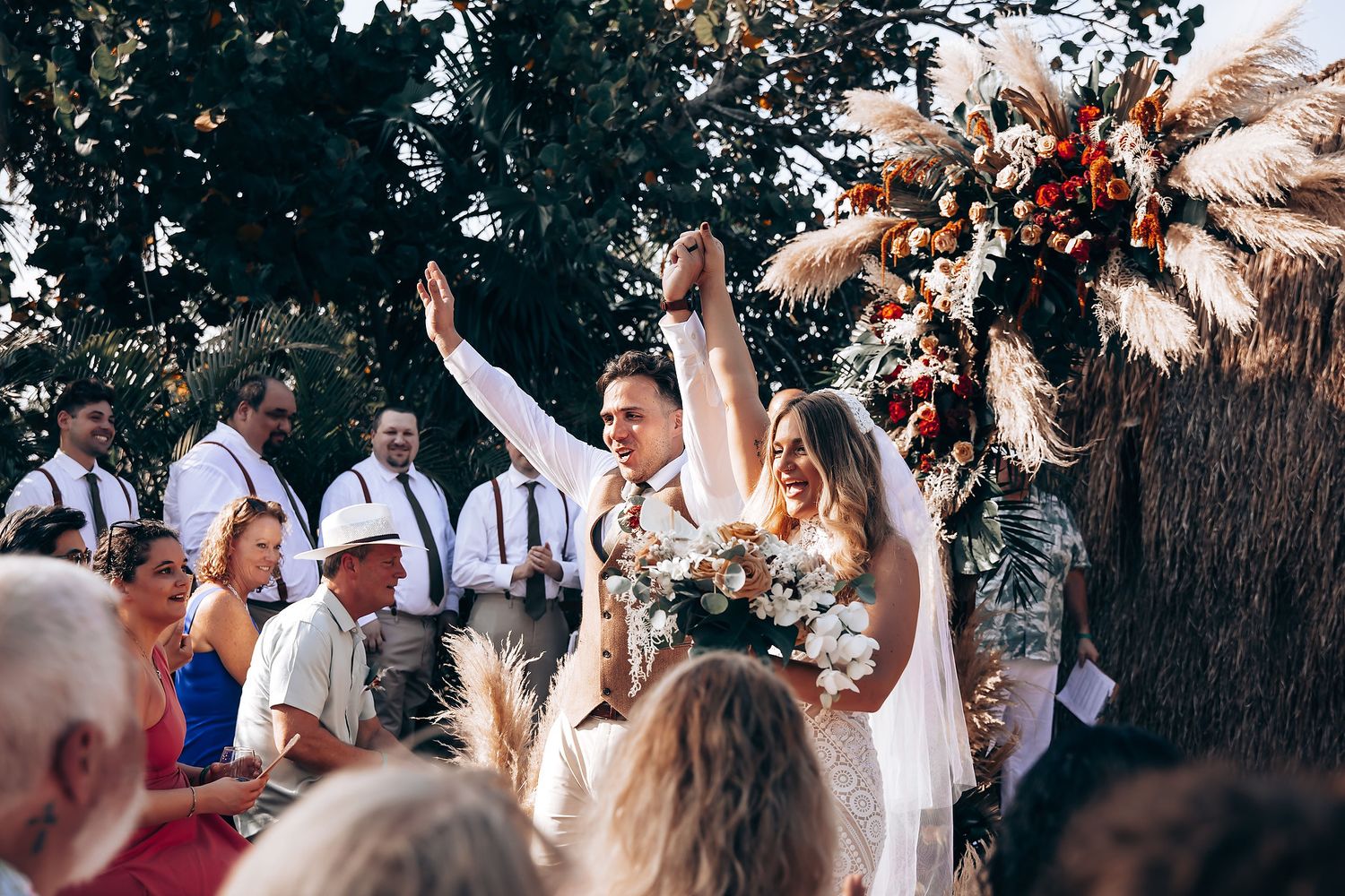 Joyful wedding celebration with guests dancing in an outdoor tropical setting.
