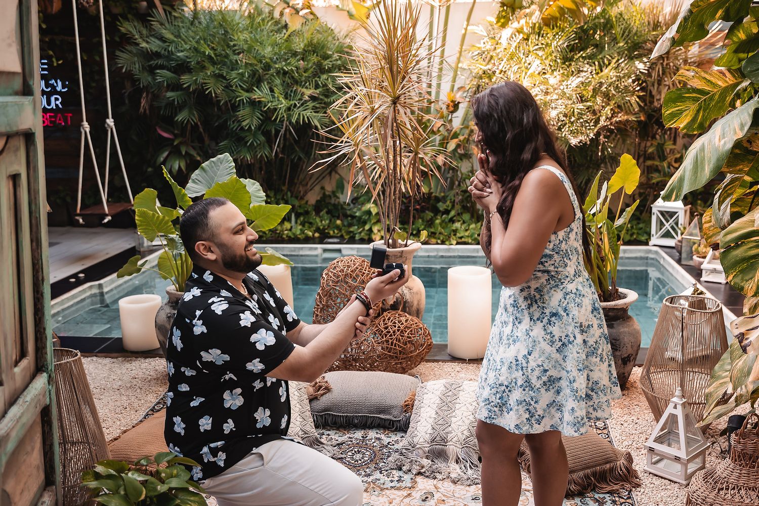 A romantic proposal scene in a lush tropical garden setting at sunset.