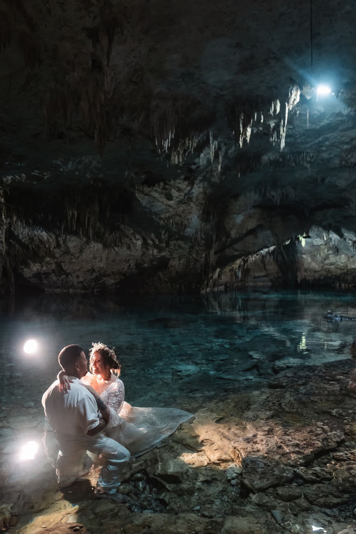 Dramatic cave photography with stalactites and turquoise waters illuminated by spotlights.
