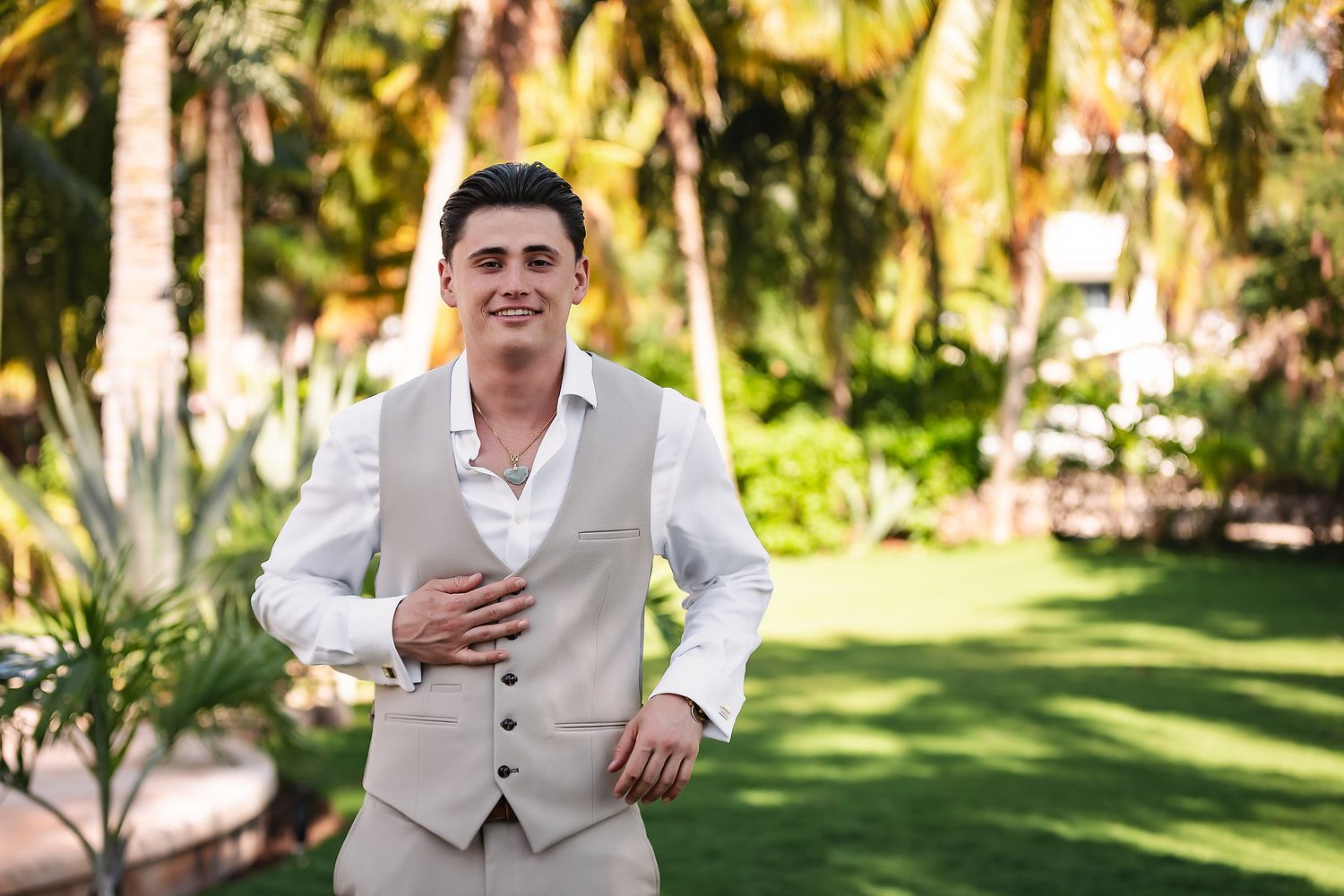 Groomsmen in light colored suits pose outdoors in a tropical garden setting.
