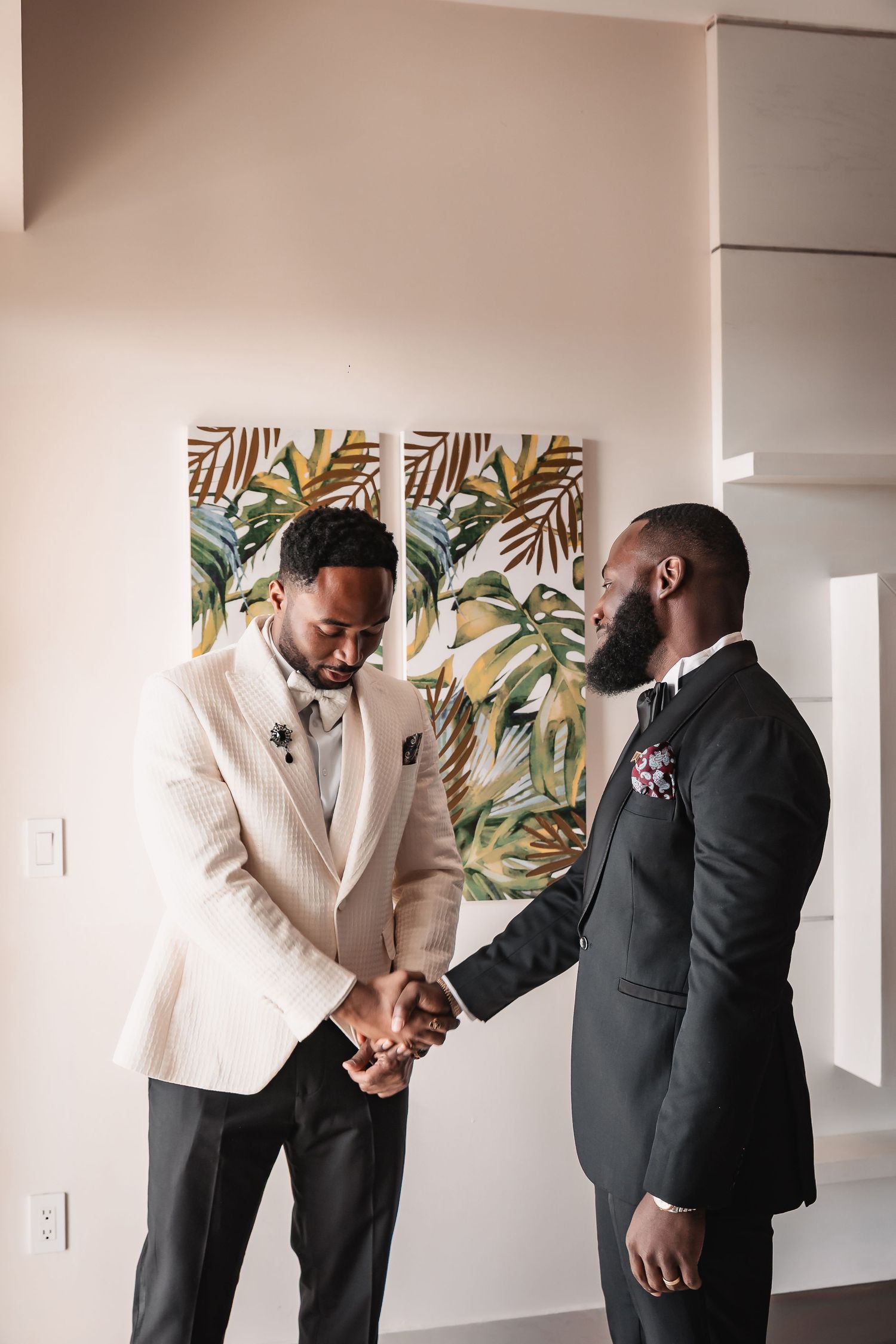 Wedding preparation scene with cream and black formal attire against tropical wall art.