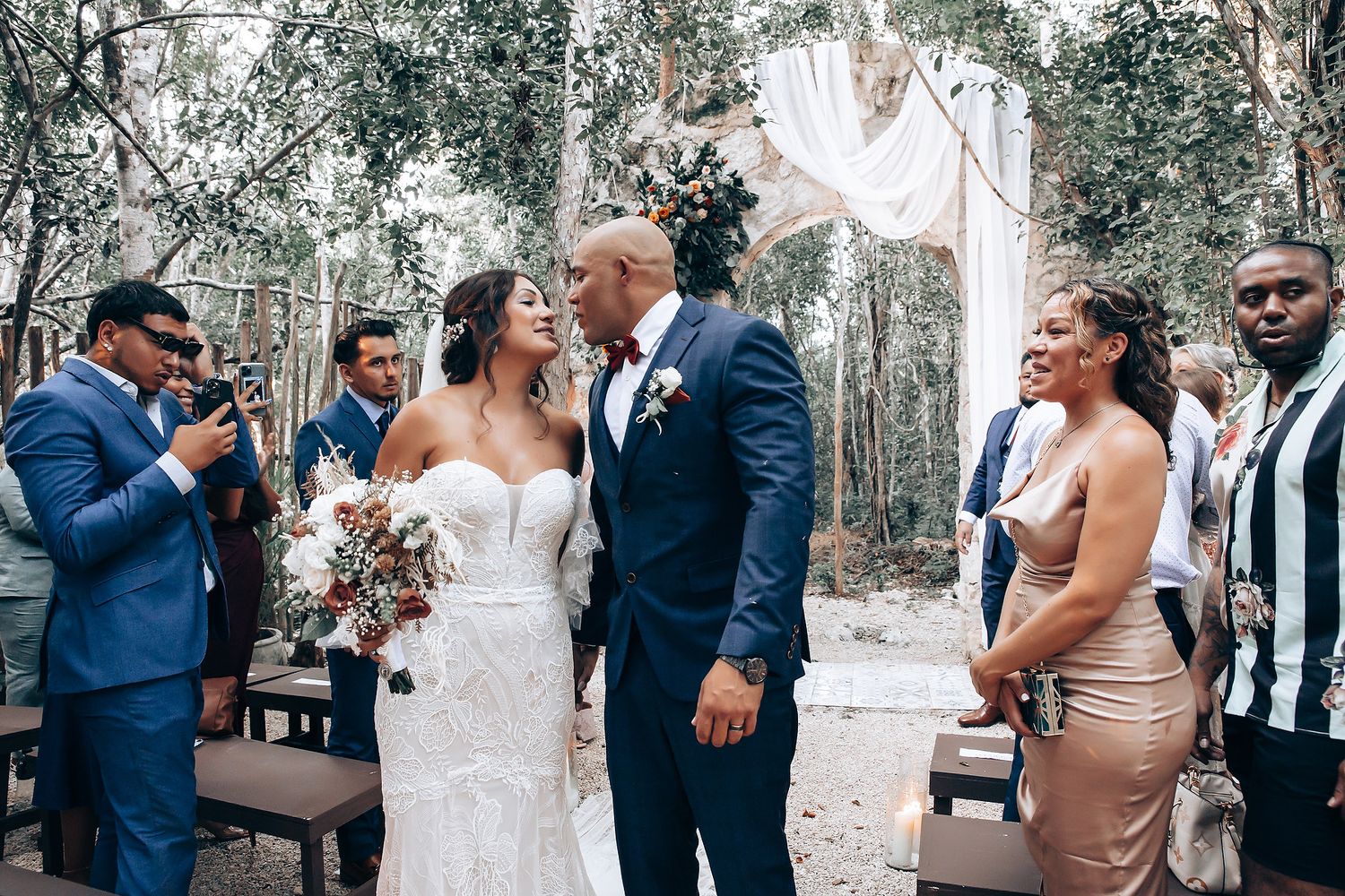 Wedding party celebrating during an outdoor ceremony with elegant white drapery and natural surroundings.