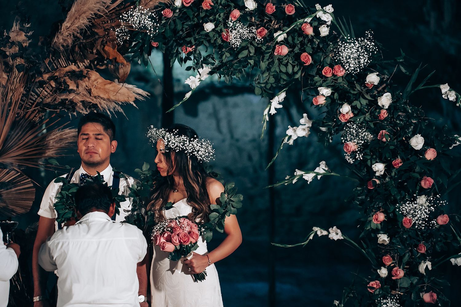Wedding couple poses in a garden setting with pink roses and moody lighting creating an enchanted atmosphere.