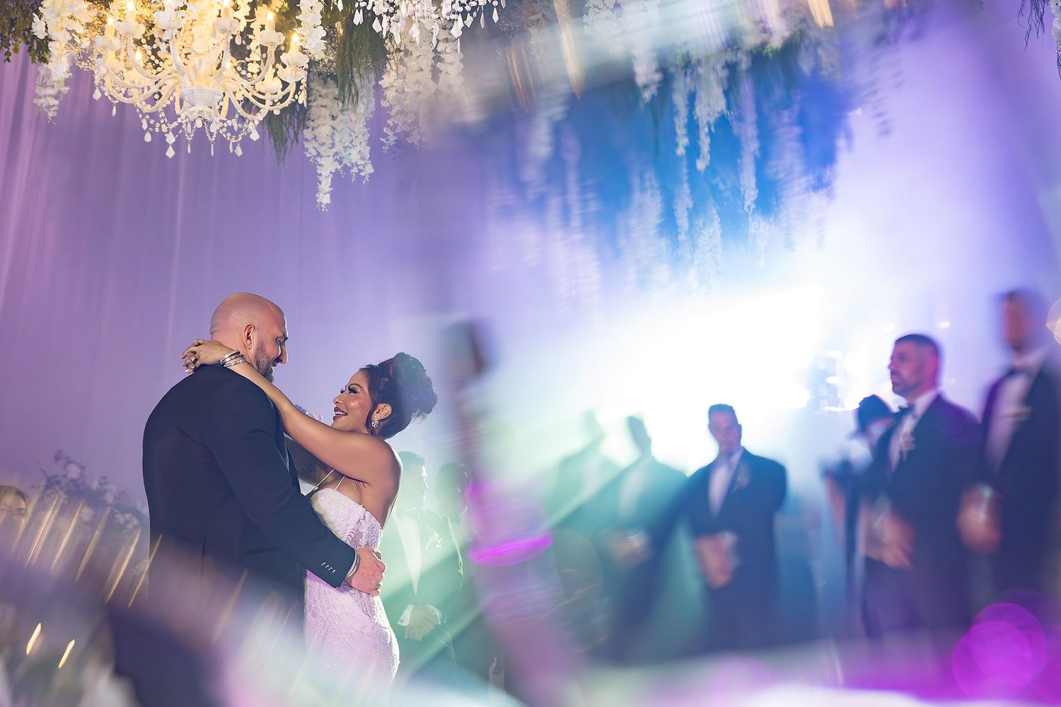 Wedding reception dance floor illuminated with colorful lights and crystal chandeliers creating a magical atmosphere.
