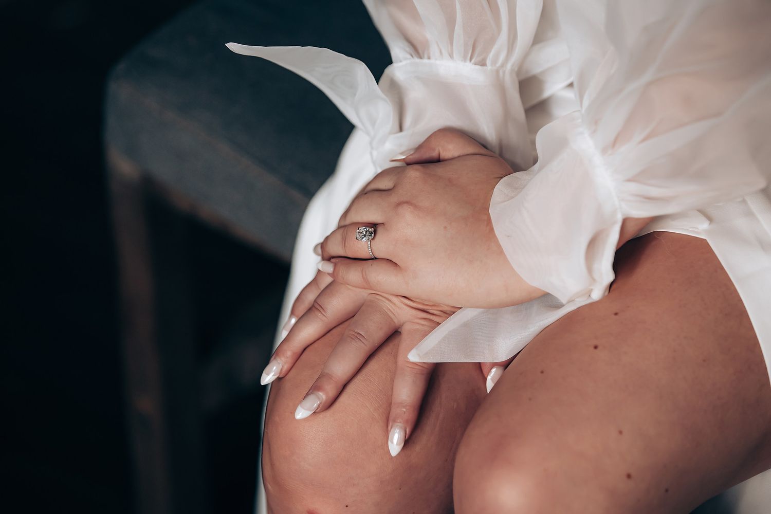 Close-up of hands with white manicure resting on knee with flowing white fabric.