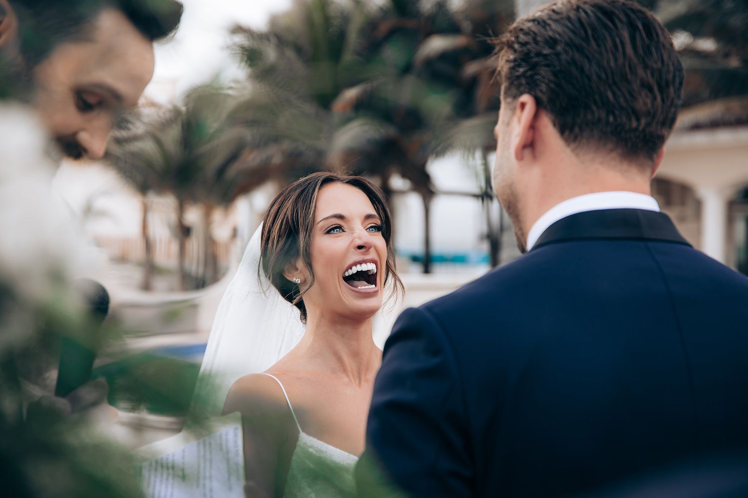 A joyful wedding celebration outdoors with palm trees and guests gathered in a tropical setting.