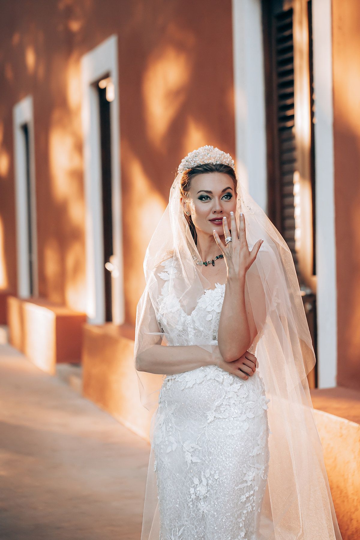 A bride in a white lace wedding dress and veil poses playfully against an orange-lit wall in a series of photos.