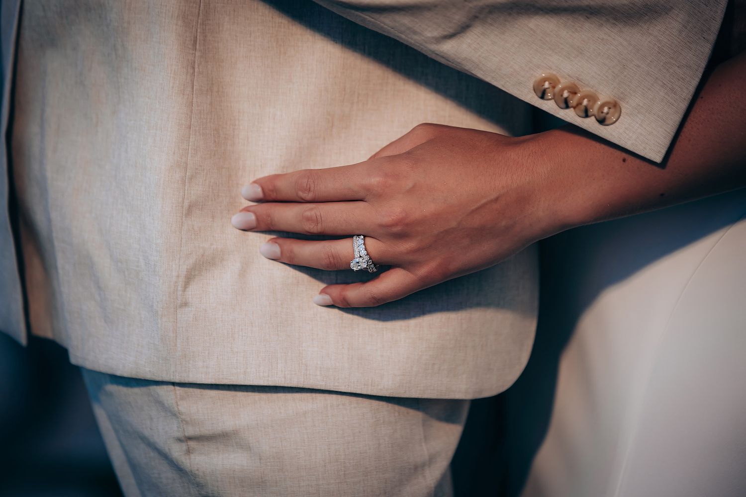 Close-up details of a wedding couple showing hands, rings, and formal attire against a blurred background.