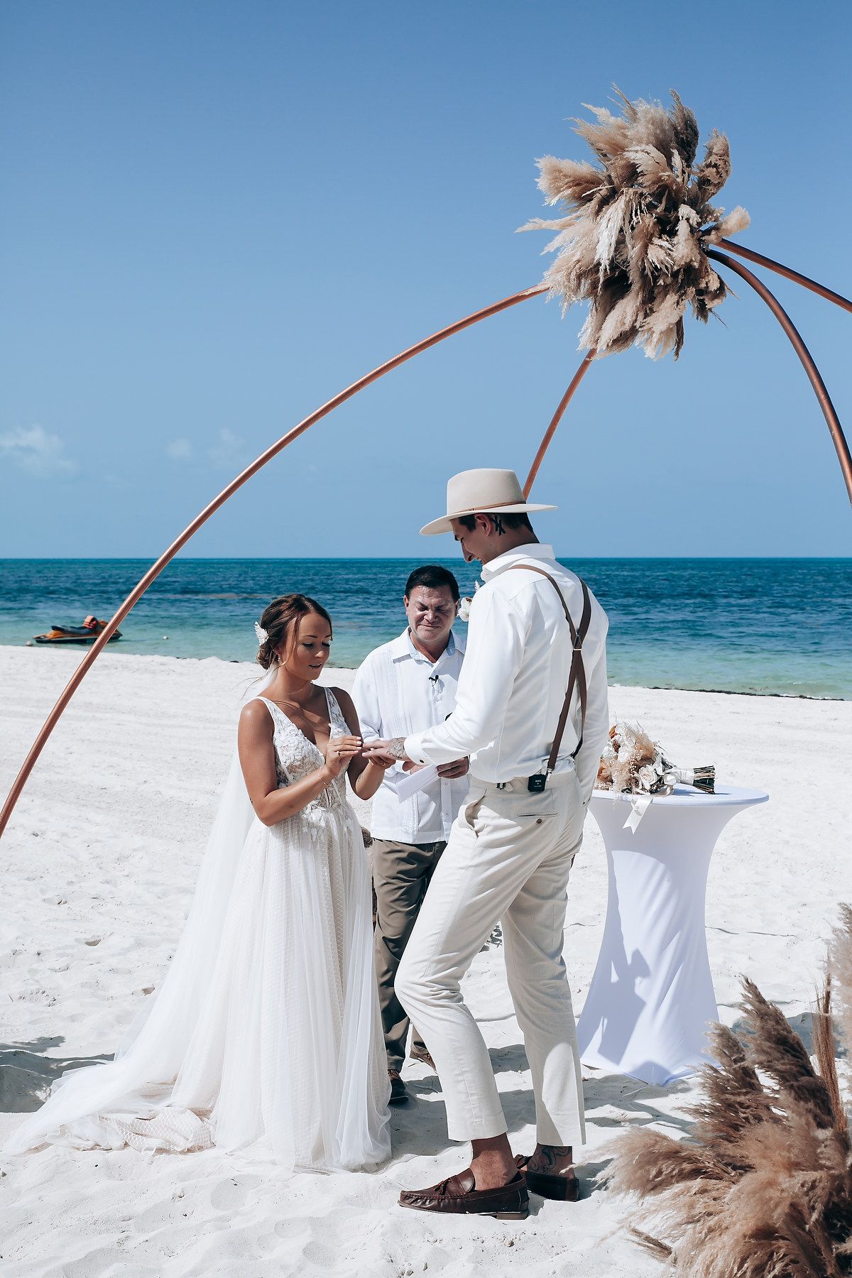 A beach wedding ceremony under an arched floral arbor with ocean views.